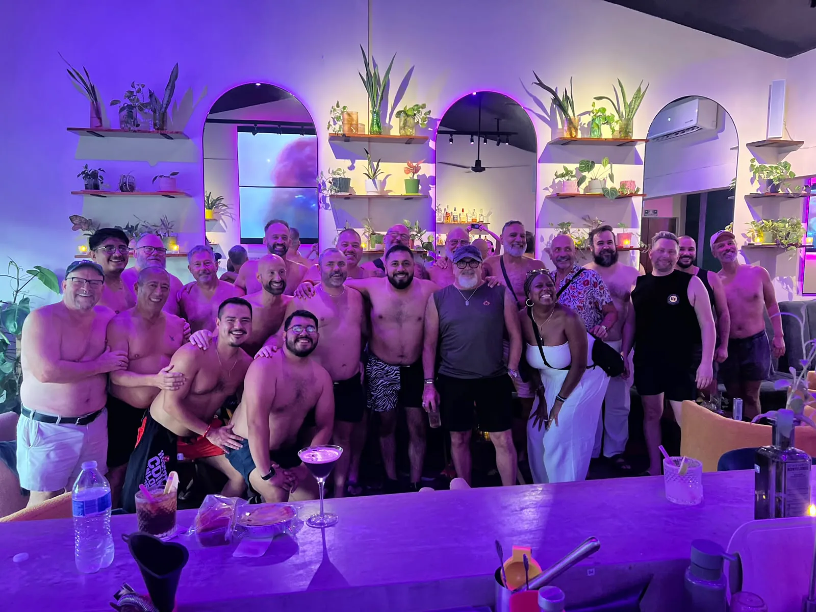 A packed Tummy Tuesday: the group crowded together at the bar, arms around each other, under purple lights.